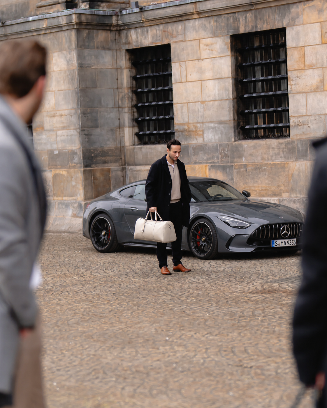 A traveller carrying the Weekender in Light Sand past a sports car